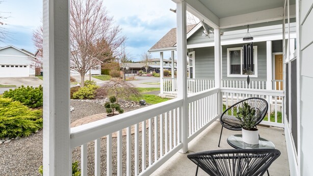 A covered porch with white railings, a potted plant, and a chair.