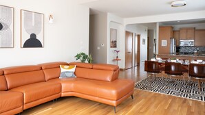 A modern living room with a leather sofa, a dining area with wooden chairs, and a kitchen with wooden cabinets.