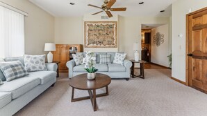 A living room with a light blue sofa, a round coffee table with a plant, a ceiling fan, and a large tapestry on the wall. - Niagara Falls Home 2BR, Pets OK, Free Parking (Niagara Falls)