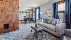A living room with a sofa, a coffee table, and a wooden cabinet. There is a dining area with a table and chairs in the background. - Niagara Falls Home 2BR, Pets OK, Free Parking (Niagara Falls)