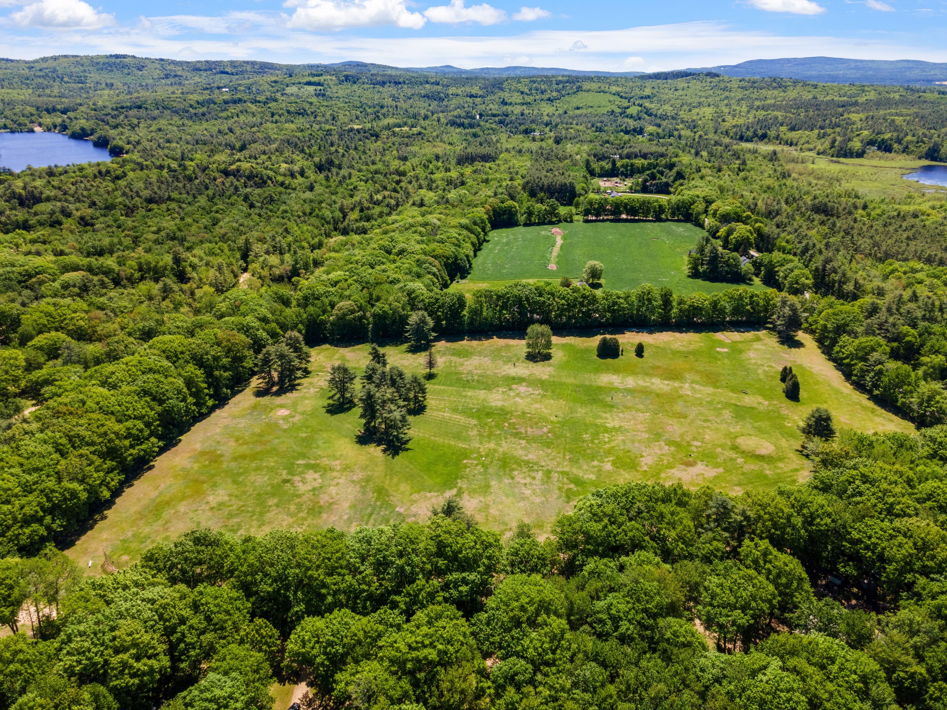 An aerial view of a large, green landscape with a central open field, surrounded by dense forest and hills in the background.