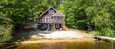 A cabin with a dock, surrounded by dense forest, near a lake.