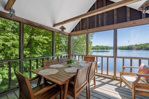 Une terrasse en bois avec une table et des chaises, donnant sur un lac et entourée d’arbres.