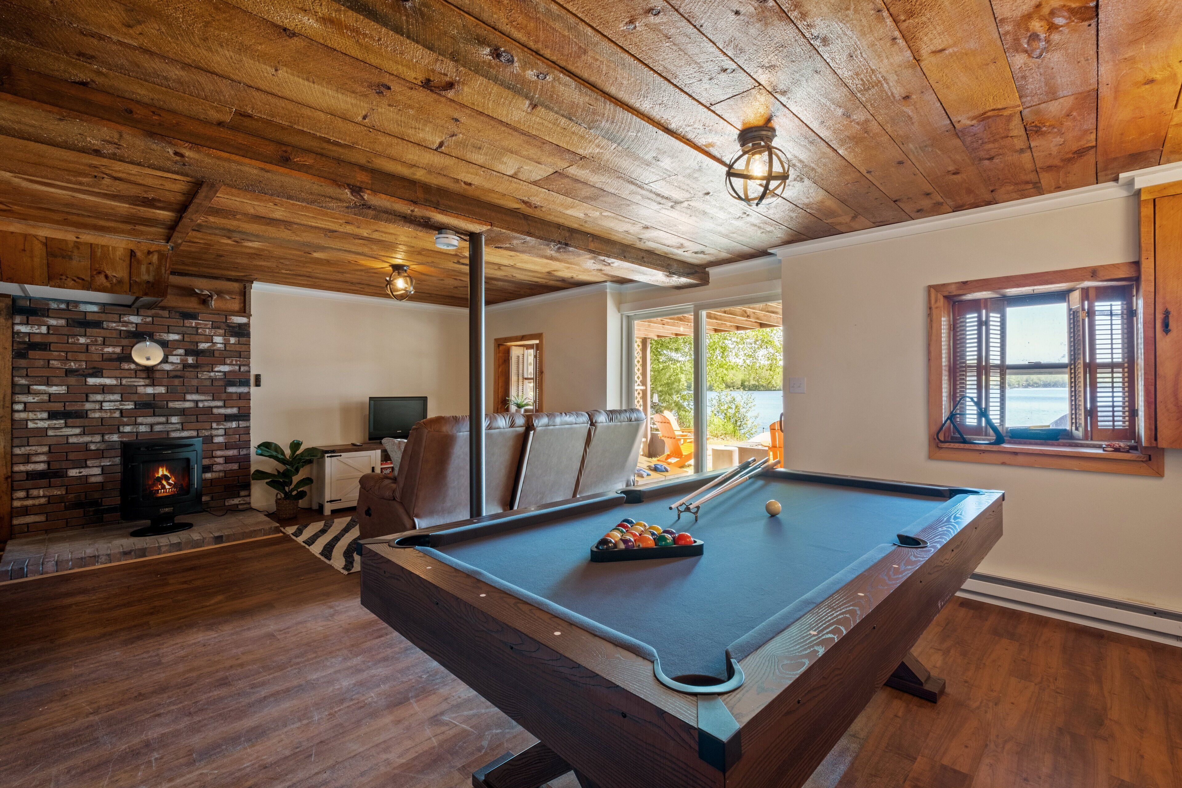 A pool table in a room with wooden flooring and a brick fireplace.