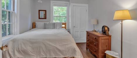 A bedroom with a large bed, a dresser, a lamp, and a window.