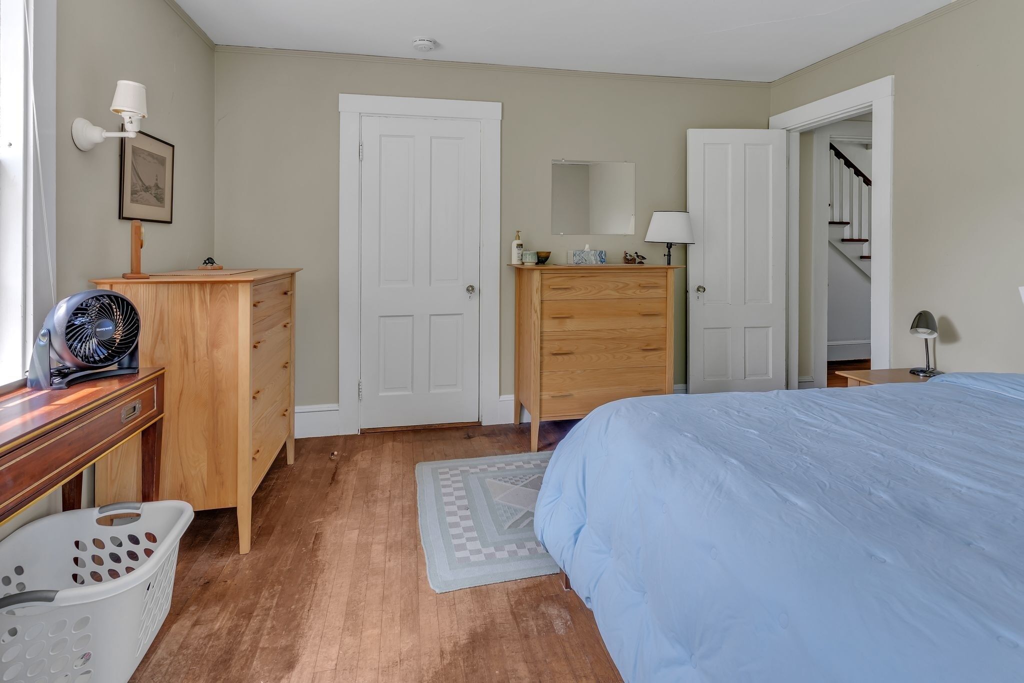 A bedroom with a bed, wooden dresser, and a desk with a fan.