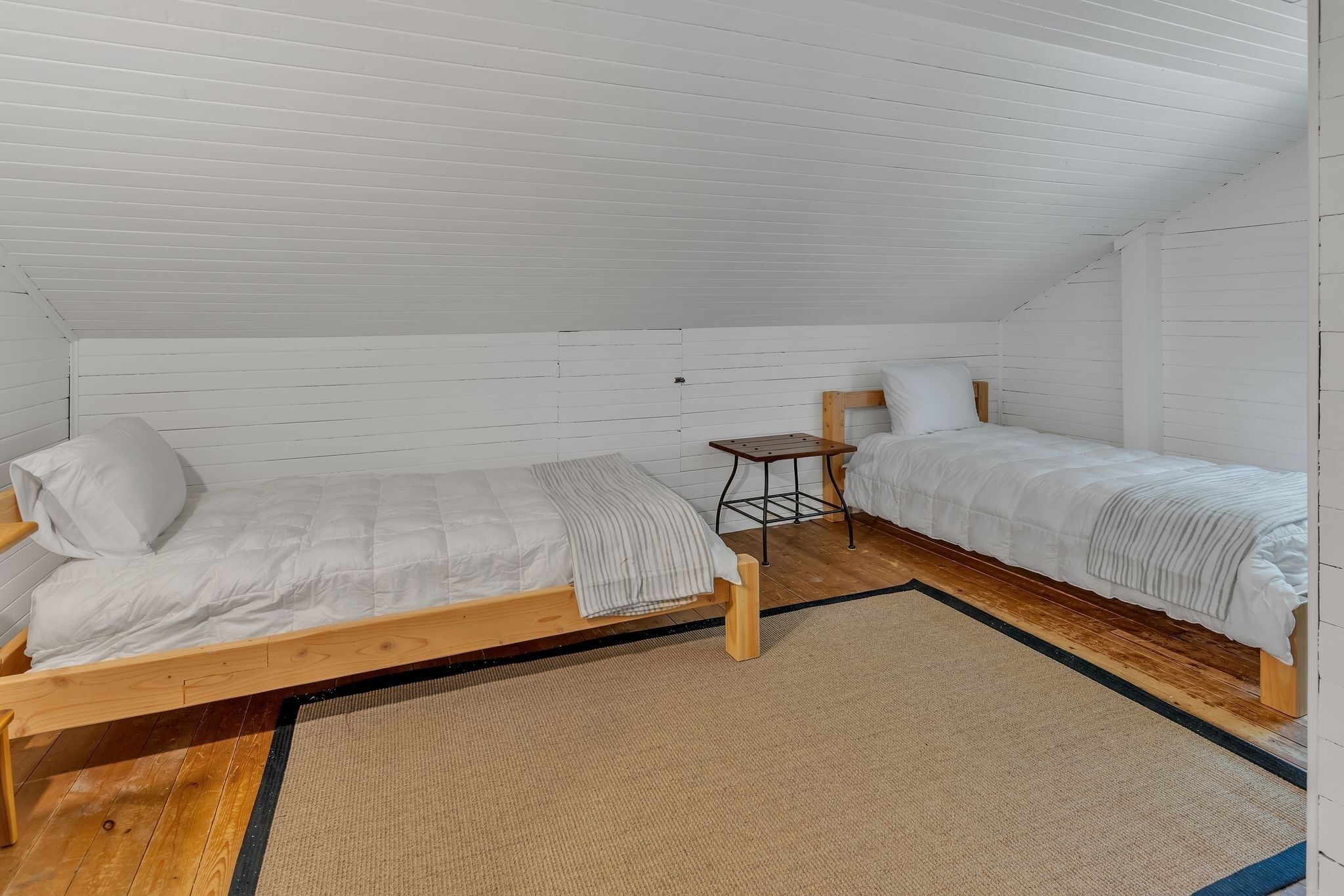 A small, single-room cabin with two wooden beds, a small table, and a window.