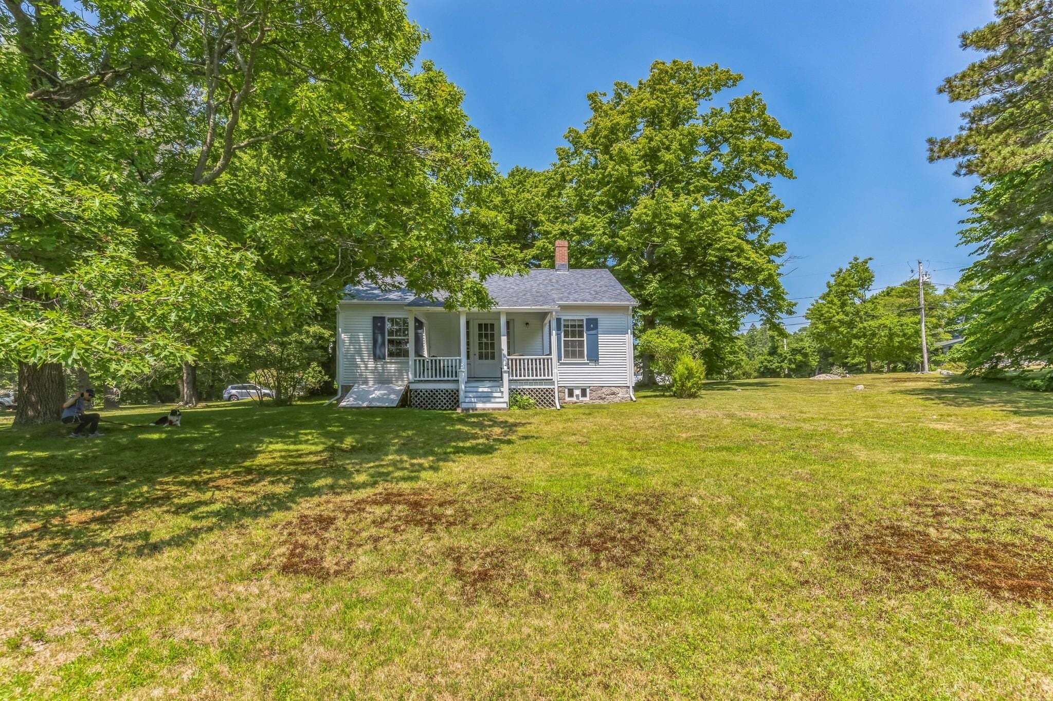 A single-story house with a porch, surrounded by a grassy yard and trees.