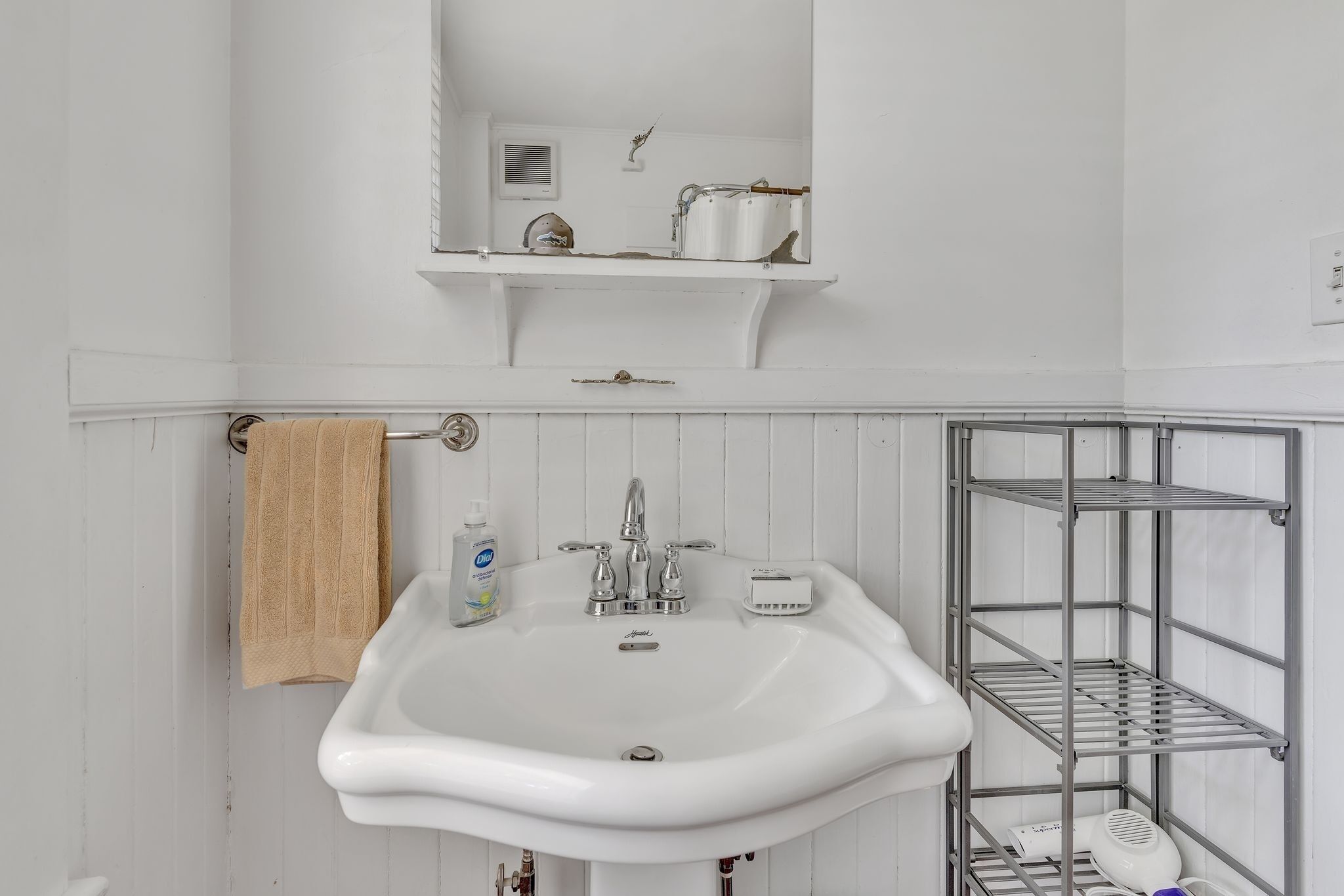 A bathroom with a white sink, a towel rack, a shelf with toiletries, and a metal storage unit.