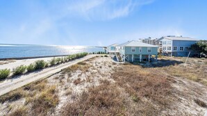 Een strandhuis met een zandpad dat naar een woning leidt, met een balkon met uitzicht op de oceaan.