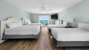 Een hotelkamer met twee bedden, een plafondventilator, een televisie en uitzicht op de oceaan.