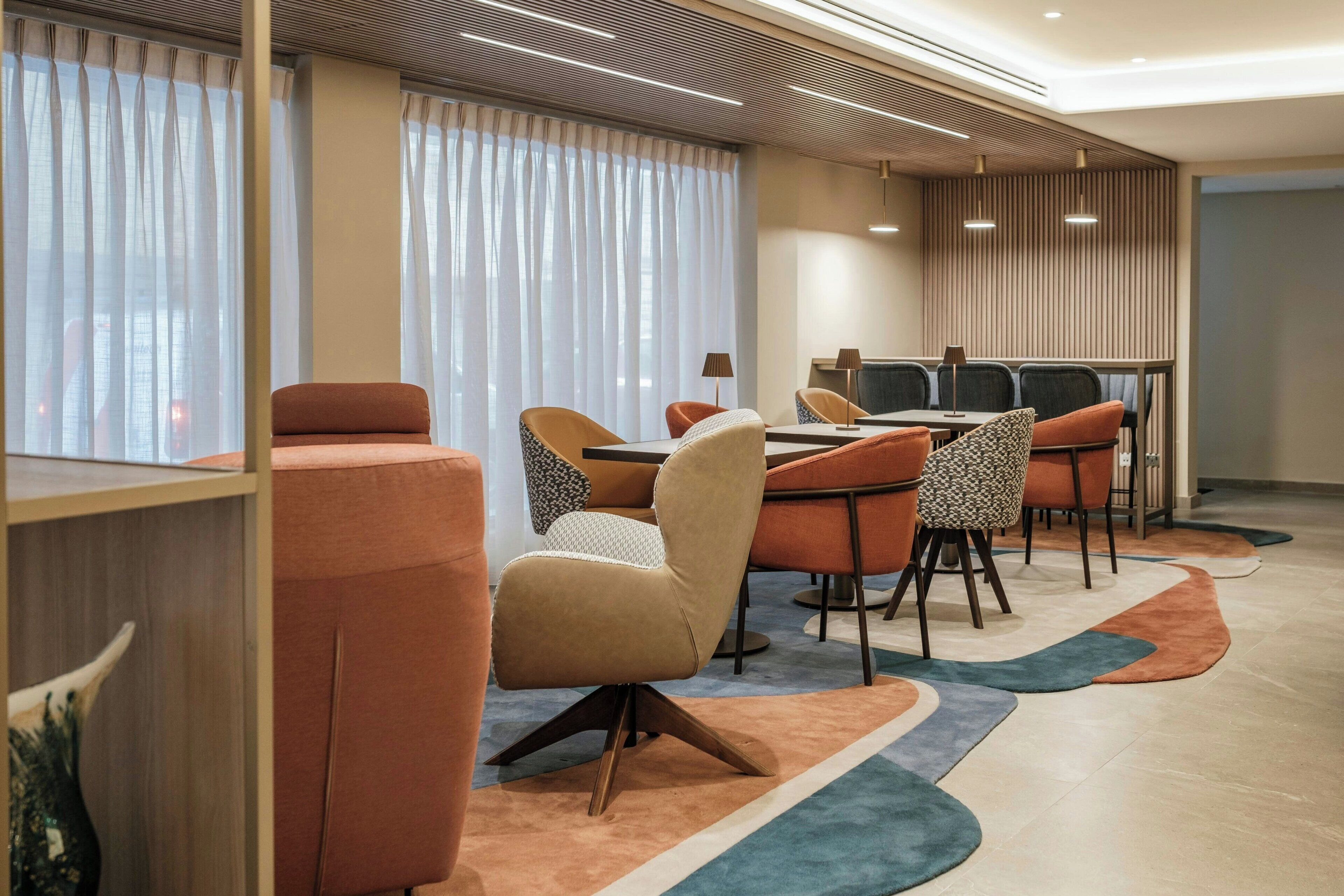 A modern conference room with a round table, orange and beige chairs, and a patterned rug.
