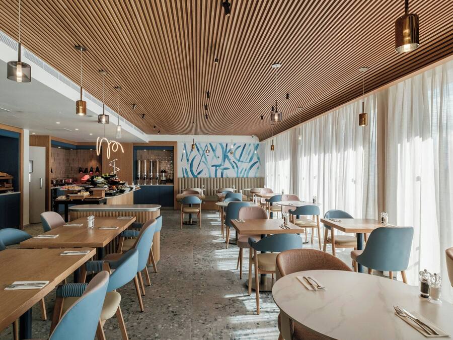 Un restaurante moderno con paneles de techo de madera, sillas azules y una zona de bar.