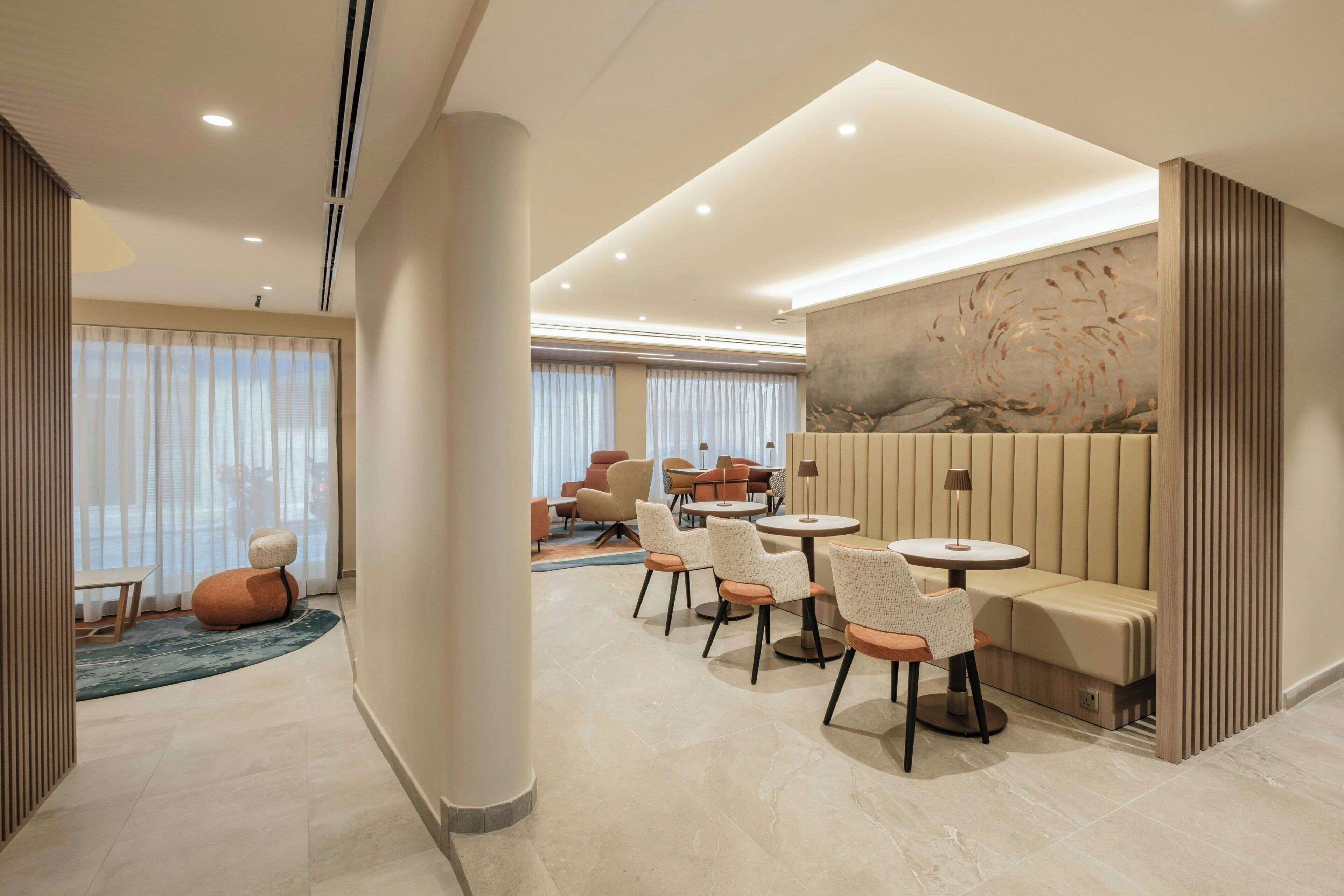 Un hall d’hôtel moderne avec un espace salon, une grande fenêtre avec des rideaux et un mur au motif texturé.