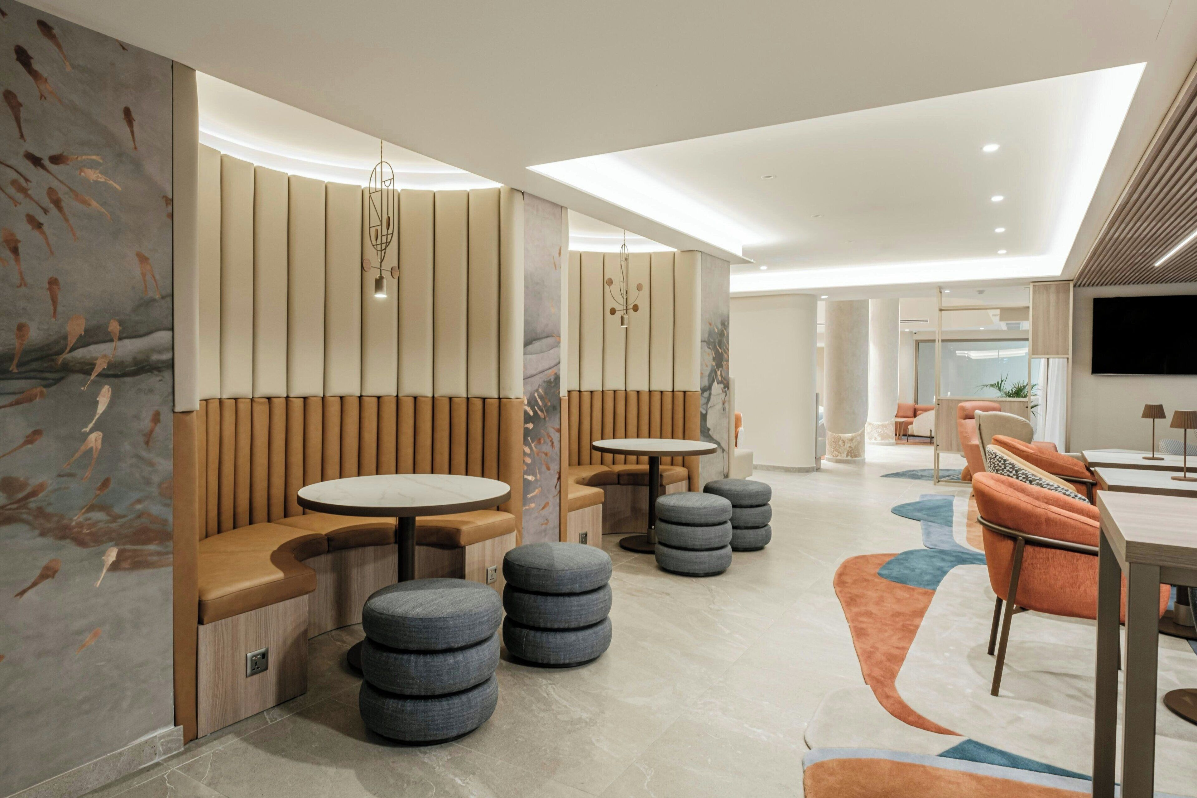 A modern interior with seating areas, round tables, and a flat-screen TV mounted on the wall.