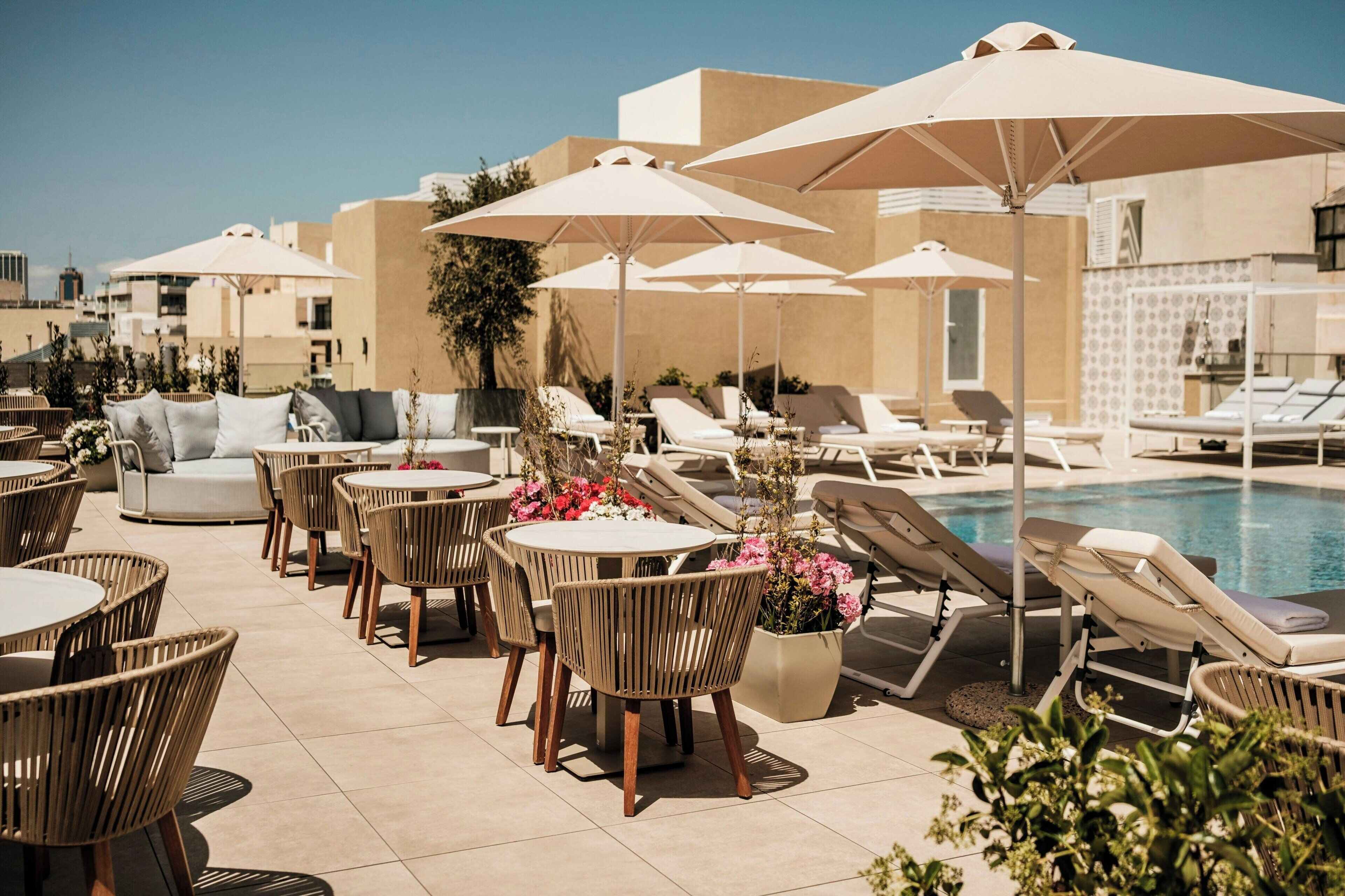 A rooftop pool area with lounge chairs, umbrellas, and dining tables.