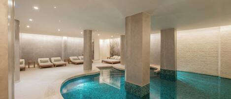 A modern indoor pool area with a curved design, lounge chairs, and a tiled floor.