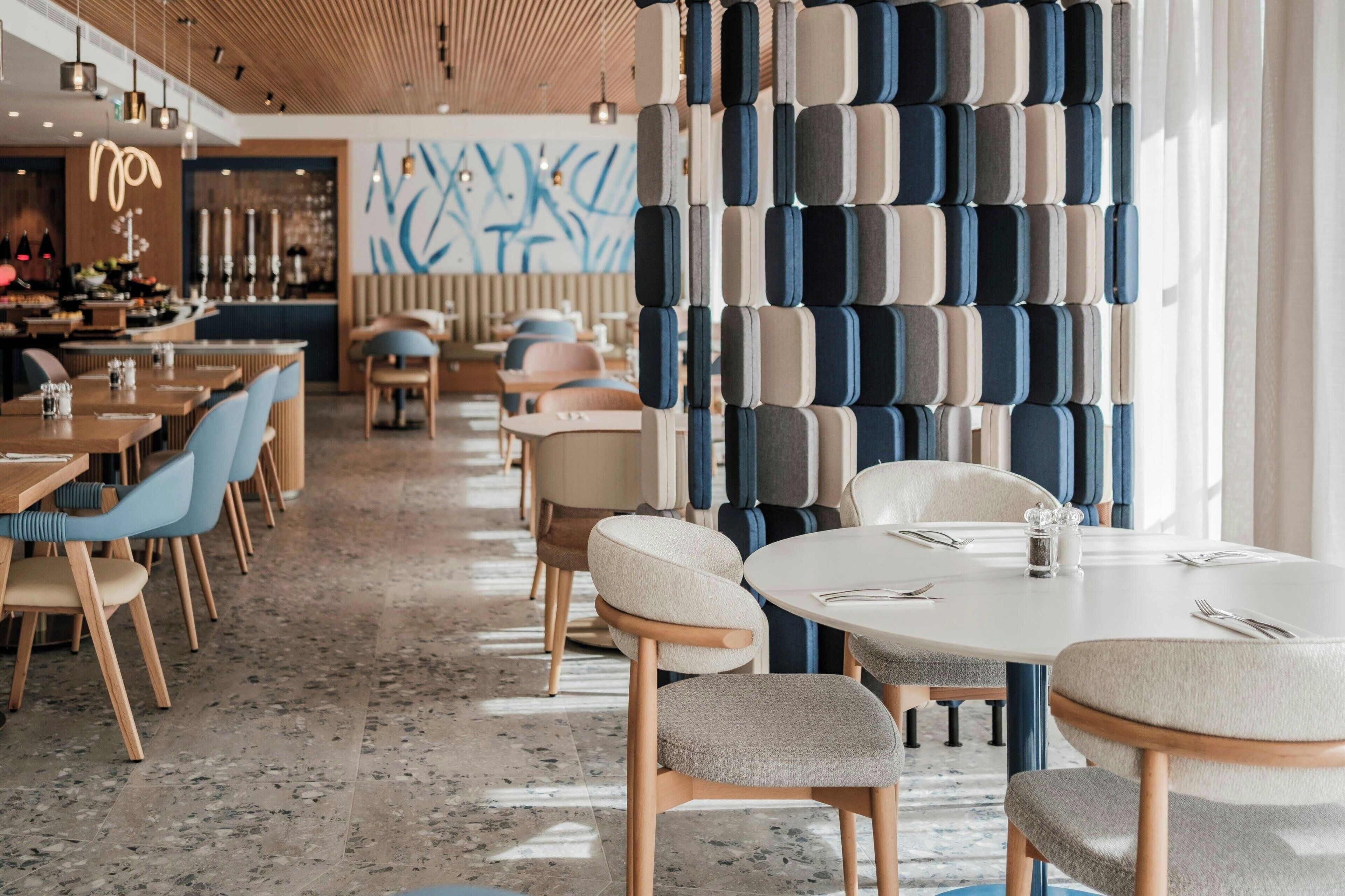 A modern restaurant interior with round tables, cushioned chairs, and a patterned wall.