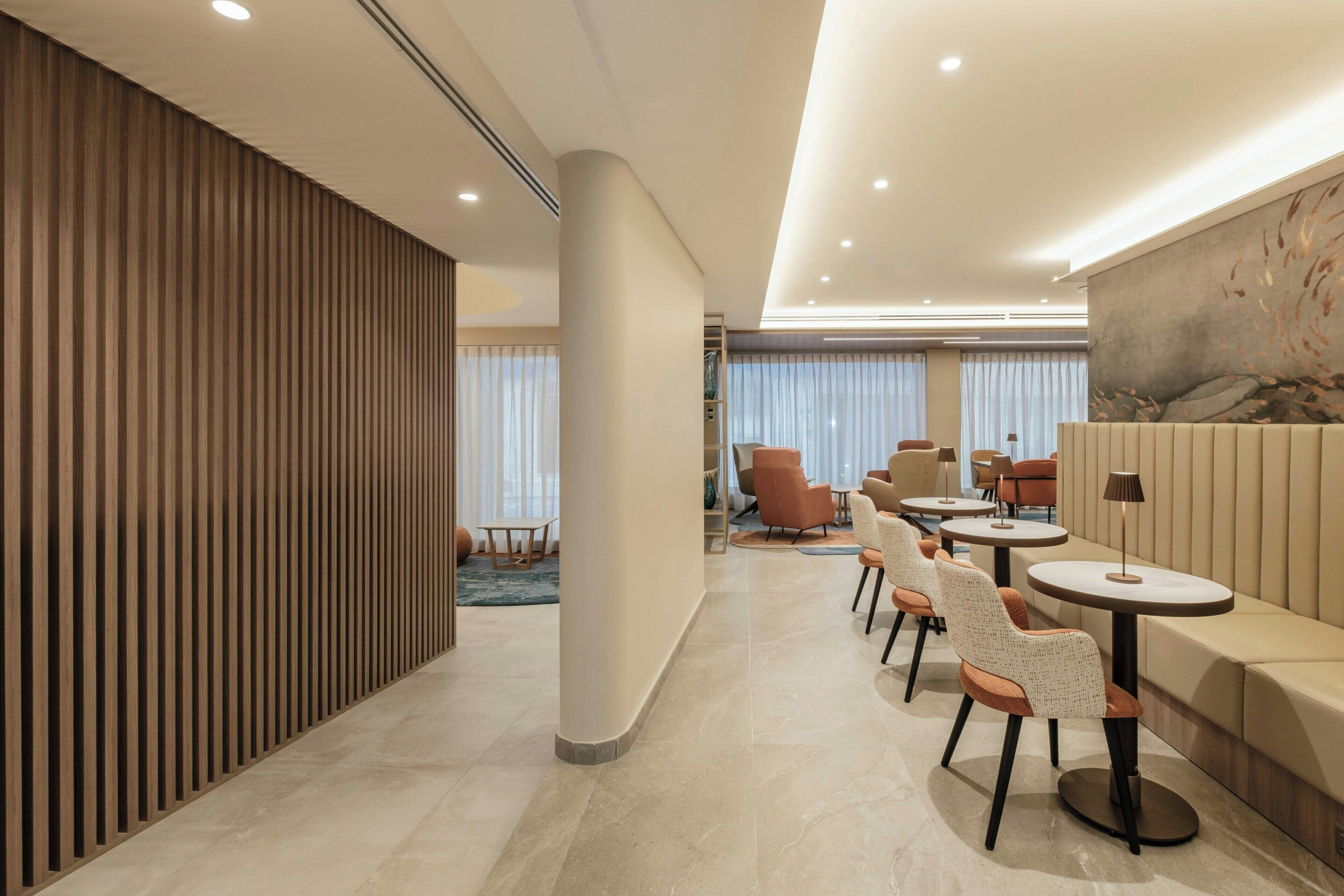 A modern hotel lobby with a long reception desk, seating area, and a large mural on the wall.