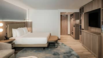 A modern hotel room with a large bed, bedside tables, a TV, and built-in storage.