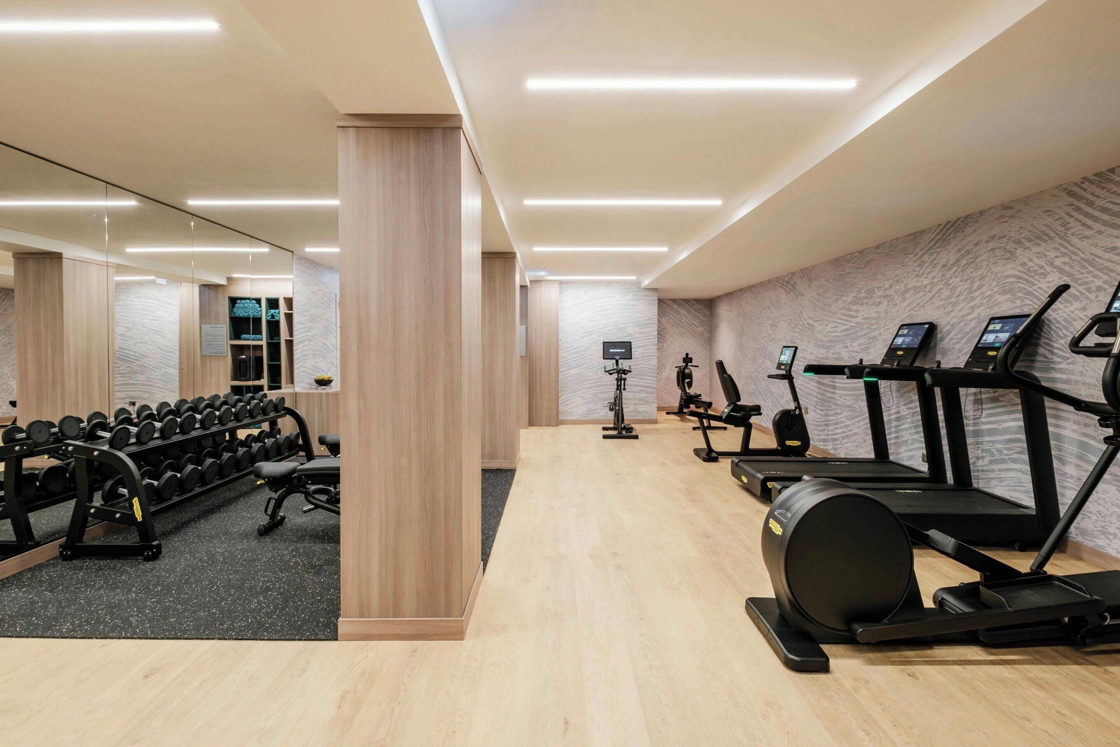 A modern gym with exercise equipment, a mirrored wall, and a wooden floor.