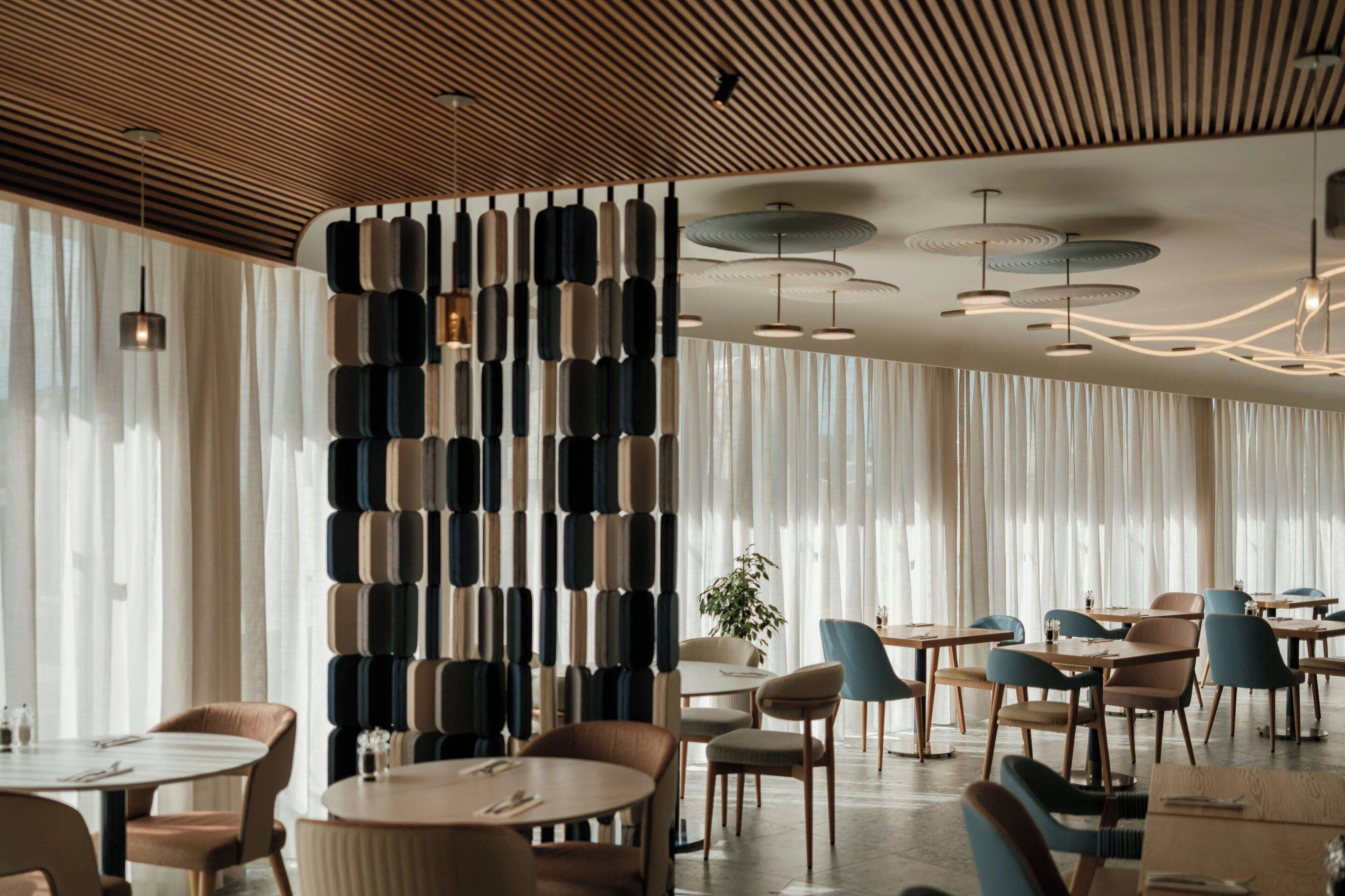 A modern dining area with round tables, chairs, and a decorative wall with vertical elements.