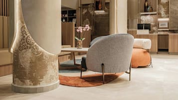A modern interior with a unique curved column, a grey upholstered chair, a small orange ottoman, and a vase with pink flowers.