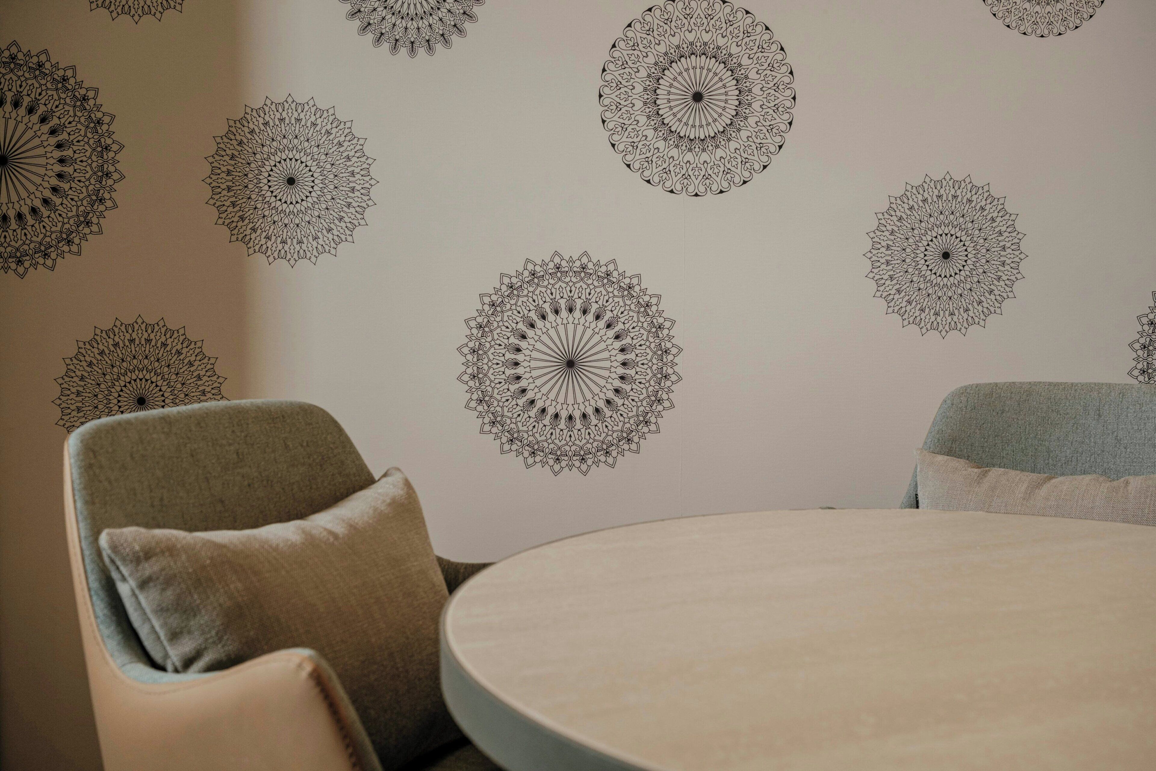A room with a round table and two chairs, a wall with circular patterns, and a light-colored wall.