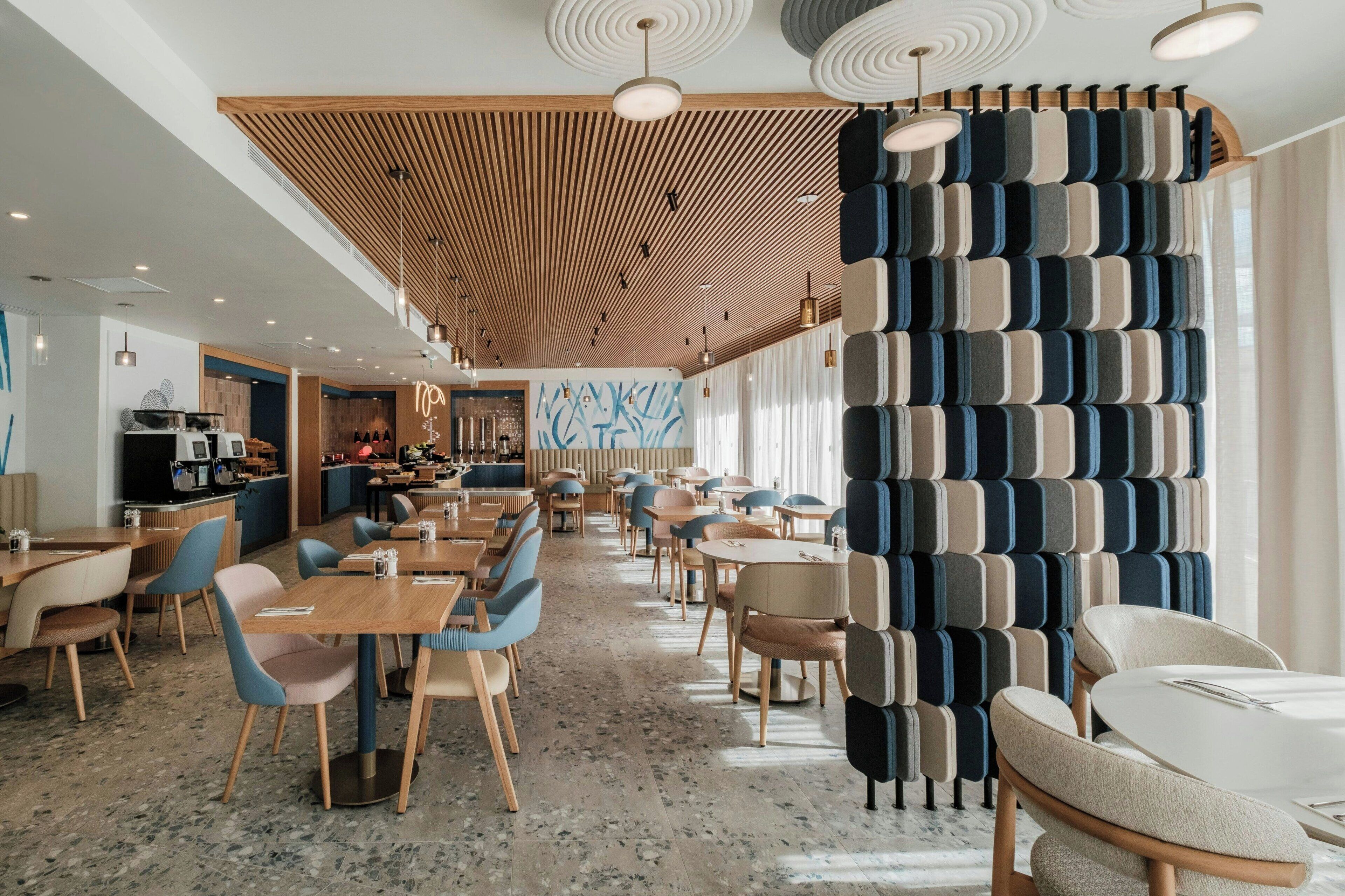 En rymlig restaurang med träpanel i taket, moderna stolar och en vägg med ett mönster.