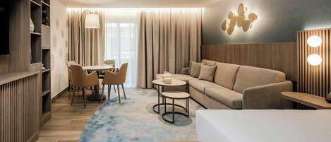 Una habitación de hotel moderna con sofá, una mesa de comedor con sillas, una mesita redonda y un televisor.
