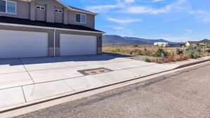 A two-story house with two attached garages, a concrete driveway, and a clear view of mountains in the background. - The Ideal Getaway 3 Bedroom Home by RedAwning (Cedar City)