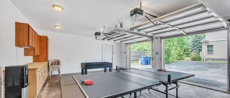 A compact living space with a ping pong table, kitchenette, and a garage door.