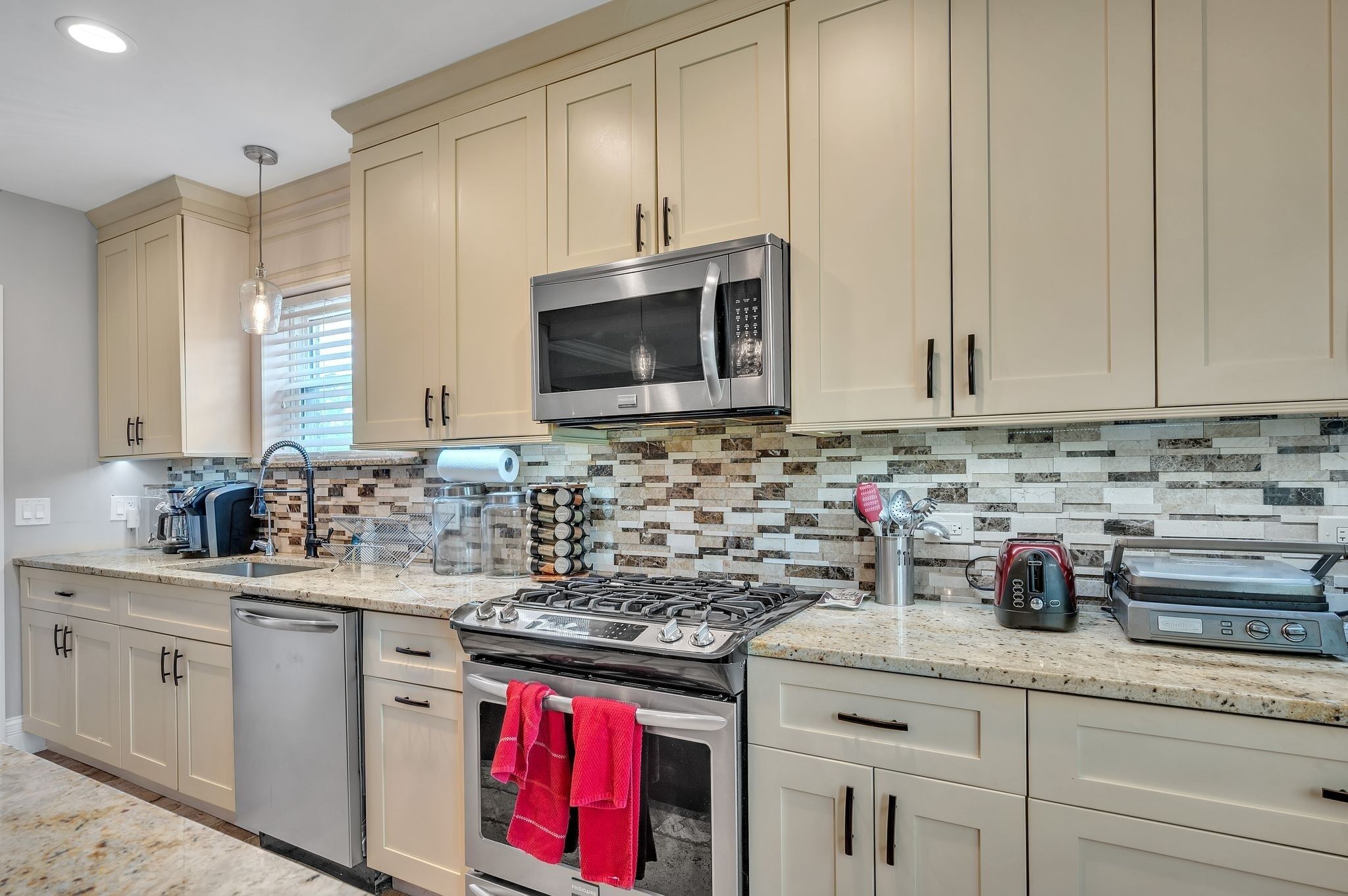 A modern kitchen with beige cabinets, a stainless steel microwave, a gas stove, and a dishwasher.