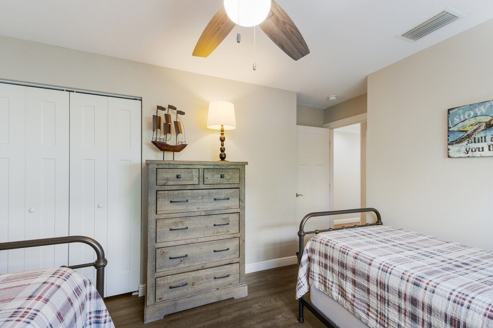A bedroom with two beds, a dresser, a ceiling fan, and a wall-mounted lamp.