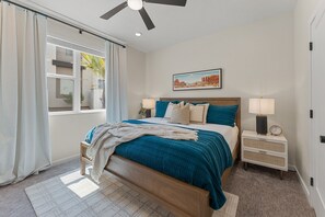 A bedroom with a bed, nightstands, a ceiling fan, and a window with curtains. - Deja Blue At Desert Color 2 Bedroom Condo (St. George)