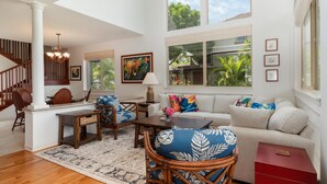 A spacious living room with a staircase, a dining area, and a large window with a view of greenery. - Big Island Golf Villas A1 3 Bedroom Condo (Kamuela)