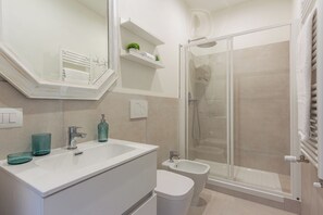Ein modernes Badezimmer mit einem weißen Waschbecken, zwei Glasvasen, einem Spiegel, einer Duschkabine und einer Toilette.