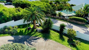 A residential area with a paved driveway, palm trees, and a view of a body of water and distant buildings. - Charming spacious 3-bedroom villa with panoramic views of Orient Bay Beach.

 (Mont Vernon)