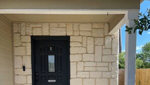 Una casa con puerta negra, fachada de piedra color beige y un cartel de bienvenida.