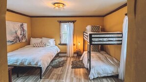 Una habitación con dos camas, una ventana con cortinas, una mesita con lámpara y un cuadro en la pared.
