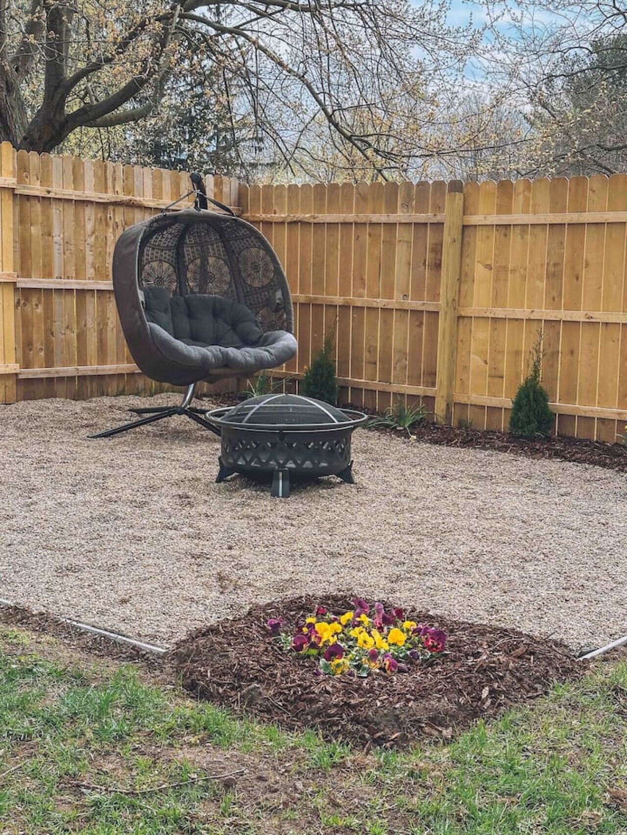 A backyard with a hanging chair, a small table, and a flower bed.