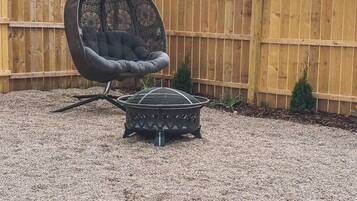A backyard with a hanging chair, a small table, and a flower bed.