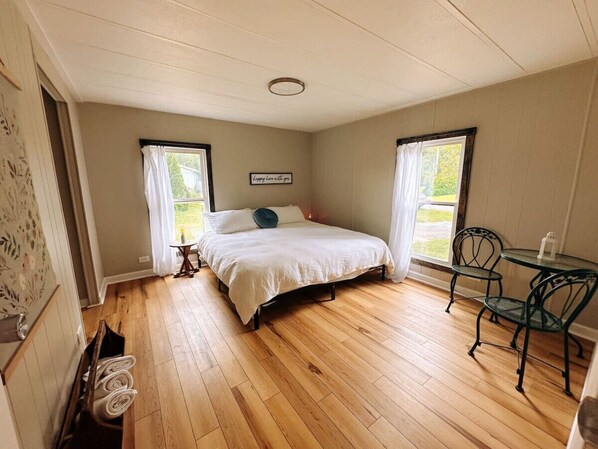 A bedroom with a bed, two chairs, a small table, and a window.