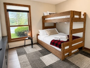A bunk bed with a window view, a small table, and a patterned rug.