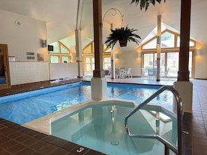 An indoor swimming pool with a separate hot tub area, clear glass walls, and a view of the outside.