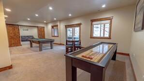 A pool table in a room with a carpeted floor, a sofa, and a window with wooden frames. - Beautiful New Home with Views of Castle Mountain - 3510 (Estes Park)