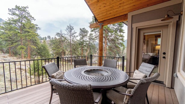 A covered outdoor patio with a round table and wicker chairs, overlooking a forested area. - Beautiful New Home with Views of Castle Mountain - 3510 (Estes Park)