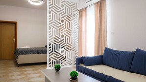 A modern living room with a sofa, a coffee table with plants, a decorative partition, and a bed in the background.