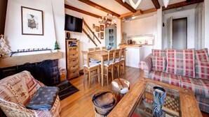 Un accogliente soggiorno con pavimento in legno, un divano, un tavolino da caffè e un camino. C'è una zona pranzo con tavolo e sedie, e una cucina sullo sfondo.