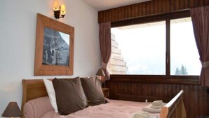 Una camera da letto con una testiera in legno, un letto con biancheria a righe, un quadro incorniciato appeso al muro e una finestra con tende.